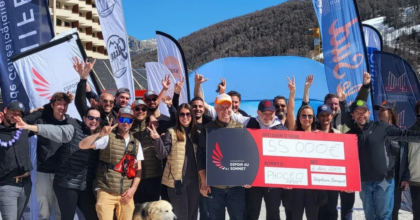 L’équipe d’Espoir au sommet et de Gliss & Mix, bras levés sur la neige, autour du chèque de 55 000 € daté du 6 avril 2025.